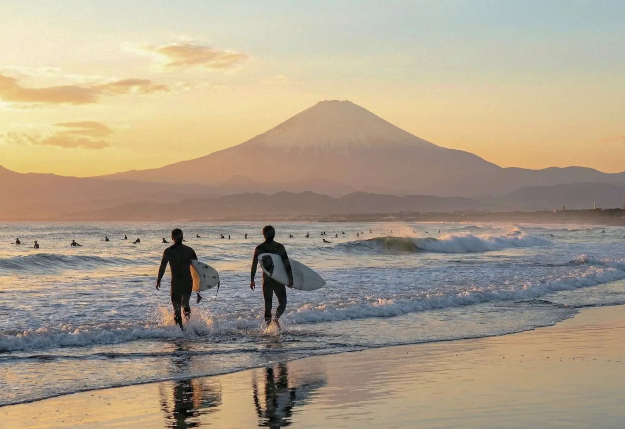 夕暮れの富士山を背に海へ入っていく2人のサーファー